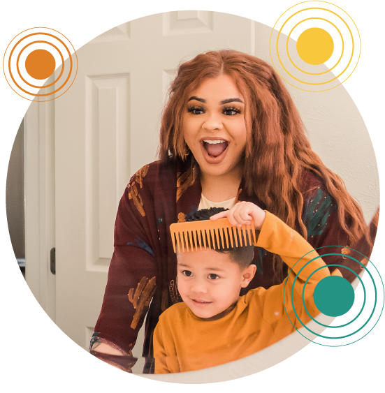 Woman with a young boy looking in a mirror smiling as the boy combs his hair.