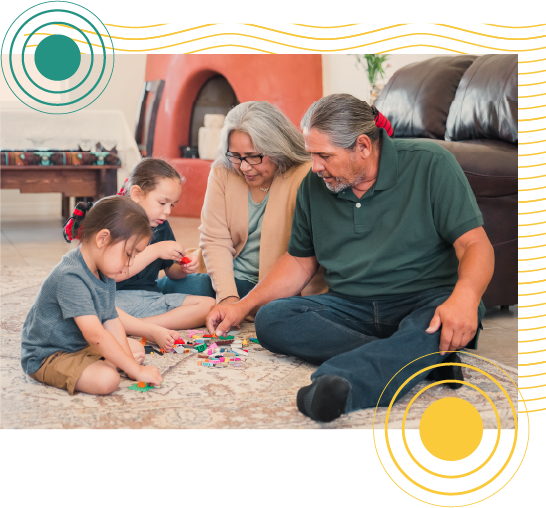 Grandparents sitting on the living room floor with two young grandchildren playing with building blocks.
